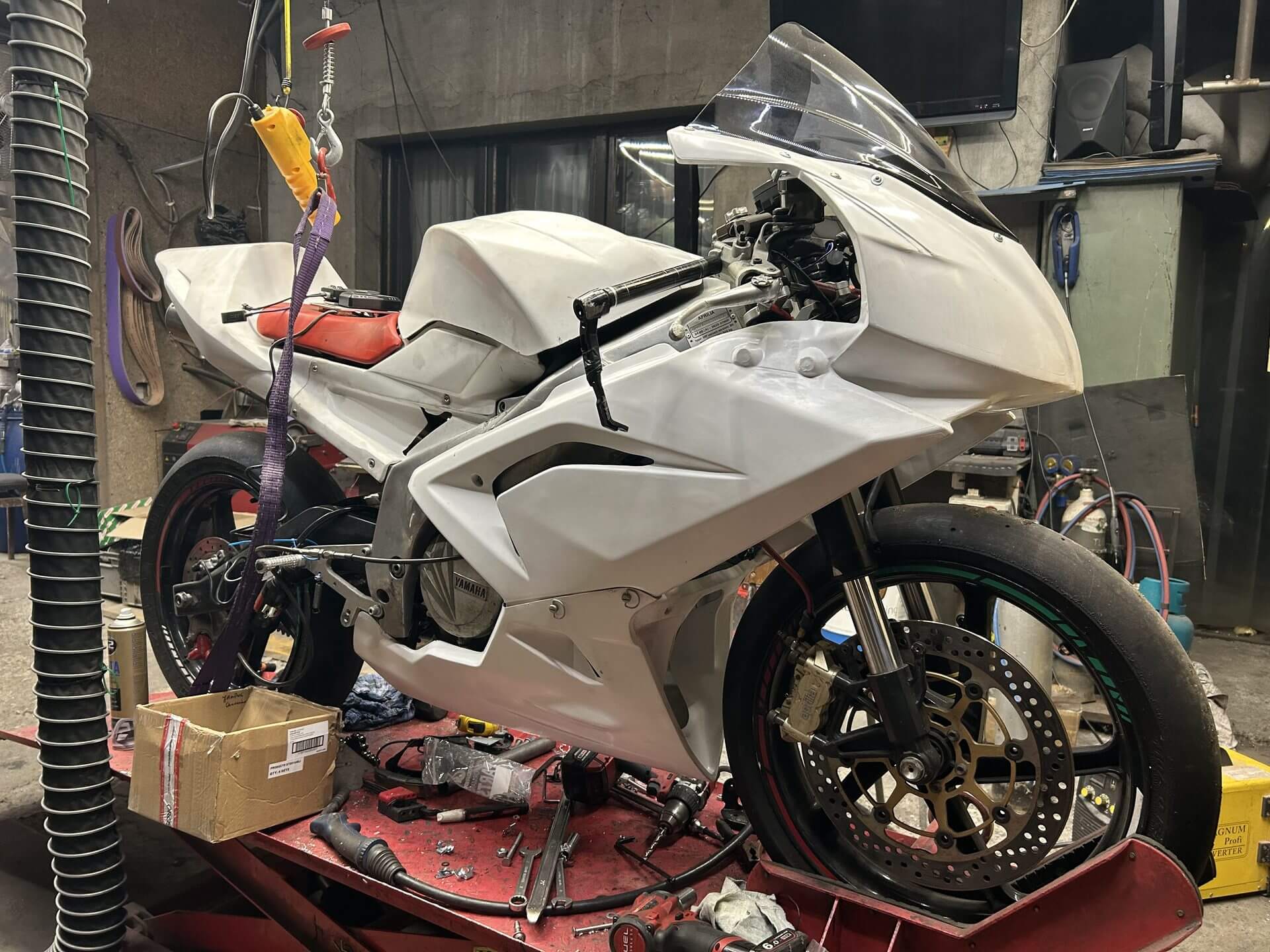Motocykl wyścigowy w białych, surowych owiewkach na podnośniku w trakcie budowy.